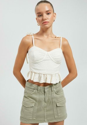 Top corto blanco con dobladillo con volantes y detalles de ojetes, tirantes delgados, combinado con una falda de mezclilla verde claro con bolsillos frontales.