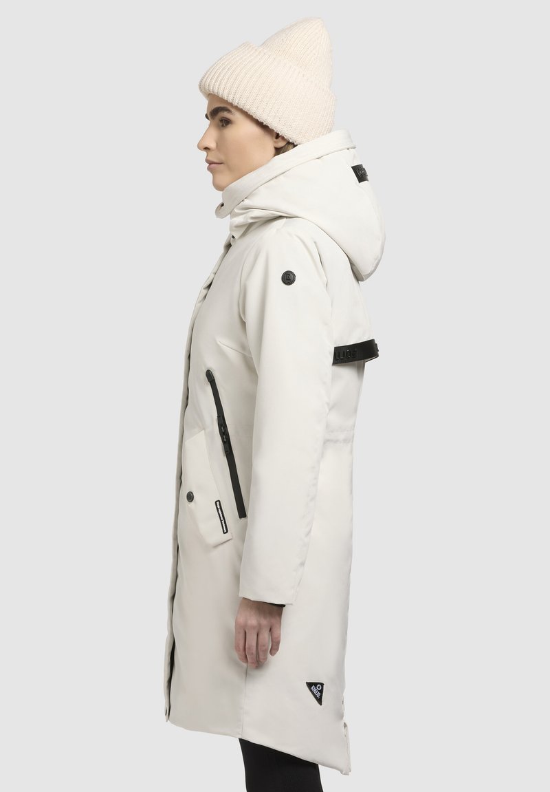 Witte waterdichte jas met capuchon, zwarte accenten en ritszakken. Gecombineerd met een geribbelde crèmekleurige beanie, slanke vorm en zachte textuur.