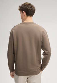 Felpa brown a girocollo realizzata in morbido cotone, con polsini e orlo a costine. Il tessuto testurizzato è liscio e presenta una vestibilità comoda.