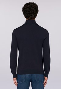 Maglione in maglia di un blu navy scuro con colletto alto, maniche lunghe e design aderente, abbinato a jeans blu. Tessuto morbido, dettagli minimi.