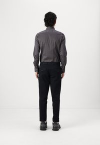 Button-up shirt with geometric pattern in dark colors, paired with dark trousers. Black shoes with textured soles. Visibility of back design.