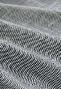 Tissu textile dans des tons de gris, présentant un motif à carreaux. Le matériau est lisse avec un léger éclat, affichant des textures ondulées sur la surface.
