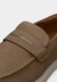 Καφέ μοκασίνι από σουέτ με μπεζ ραφές και ασημένιο λογότυπο "KARL LAGERFELD" στο λουράκι πάνω από το μπροστινό μέρος.