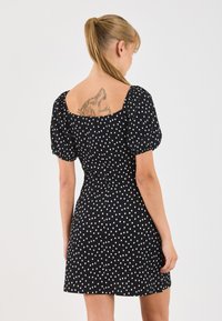 Blond hajú nő, fekete ruhában, fehér pöttyökkel, amelyen egy részletes aligátoros háttetoválás látható.