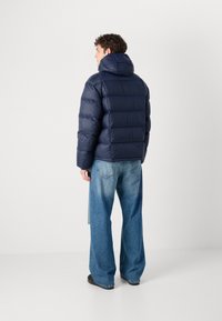 Navy puffer jacket with a hood, featuring quilted panels and a smooth texture. Worn with wide-leg blue jeans and black shoes.