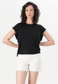 Camiseta negra corta con mangas enrolladas, hecha de un tejido suave. Combinada con pantalones cortos blancos, exhibida sobre un fondo liso.