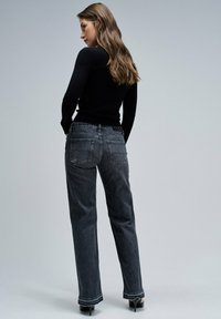 Top negro de manga larga combinado con jeans oscuros de tiro alto. Los jeans tienen bolsillos traseros y un dobladillo ligeramente deshilachado. Se llevan zapatos de tacón.