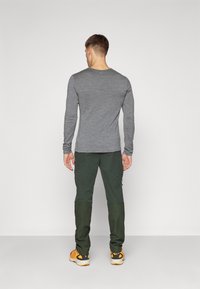 Szara koszula z długim rękawem zestawiona z ciemnozielonymi spodniami. Koszula ma gładką fakturę; spodnie mają design w blokach kolorów z kieszeniami.