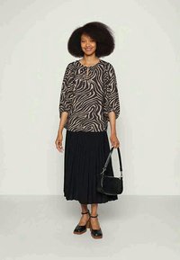 Blusa de padrão animal em preto e bege com mangas três quartos, combinada com uma saia preta plissada e uma bolsa preta; modelo a usar sandálias de salto bloco.