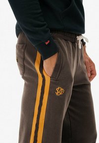 Grå sweatpants med en gul sidekant og matchende logo. Har en elastisk talje og sidelommer. Blødt, afslappet stof.