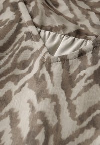 V-Ausschnitt-Bluse aus einem weichen, leichten Stoff mit einem beigen und braunen abstrakten Muster. Merkmale sind eine Nähedetail entlang des Ausschnitts und eine interessante Textur.