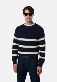 Jersey de punto a rayas en azul marino y blanco con textura acanalada y cuello redondo, combinado con pantalones de mezclilla oscuros y un cinturón negro.