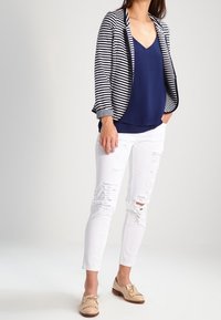 Blazer rayé bleu marine et blanc porté sur un haut bleu marine, associé à un jean blanc déchiré et des mocassins beige. Le blazer a une texture douce et une coupe décontractée.