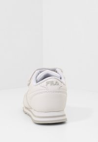 Sneaker bianco in pelle con punta tonda, fodera in mesh, cinturino regolabile e dettagli grigi sulla suola e sul logo. Superficie testurizzata sul tallone.