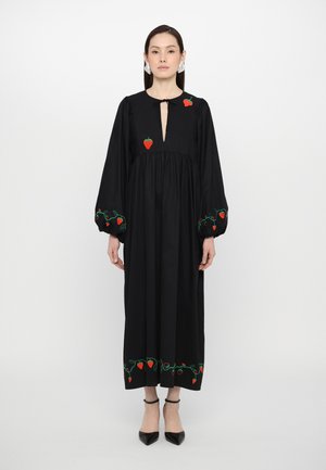 Μαύρο φόρεμα με μακριά μανίκια και κούμπωμα με άνοιγμα στην περιοχή του λαιμού. Διακοσμείται με κεντητές κόκκινες φράουλες στο στήθος, στις μανσέτες και στο στρίφωμα.