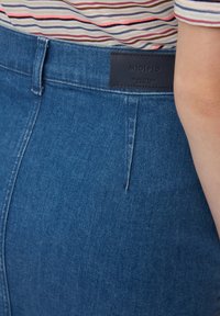 Jean en denim bleu foncé à taille haute, avec une étiquette en cuir au niveau de la taille arrière et une poche avant avec des détails de couture.