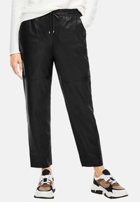 Pantalons de jogger en cuir noir avec une taille élastique, un cordon de serrage et deux poches latérales. Associés à des baskets à motifs.