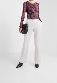 Long-sleeve bodysuit with a multicolored paisley pattern, paired with wide-leg white trousers and black pointed-toe heeled boots. Black handbag.