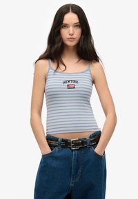 Gestreiftes Trägershirt in Hellblau mit dunkelblauen und weißen Linien; mit "NEW YORK" Stickerei und einem kleinen Flaggenlogo. Getragen mit hochgeschnittenen Denim-Jeans.