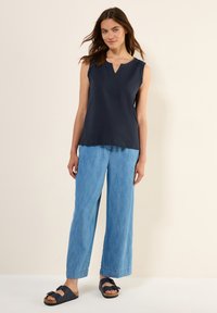 Top senza maniche di colore blu navy con scollatura a V, abbinato a pantaloni a gamba larga leggeri di colore blu chiaro e sandali neri con dettaglio fibbia.
