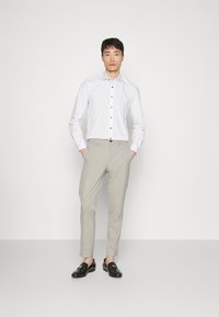 Hvid skjorte med sorte knapper, lyse beige bukser og sorte loafers med hardware-detaljer. Casual pasform med en glat tekstur.