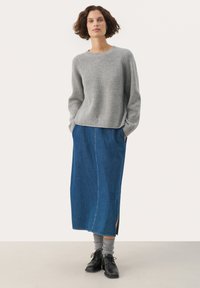 Grauer gerippter Pullover, blaue Denim-Maxi-Rock mit seitlichem Schlitz, graue Socken und schwarze Schnürschuhe. Ein einfarbiger Hintergrund hebt die Details des Outfits hervor.