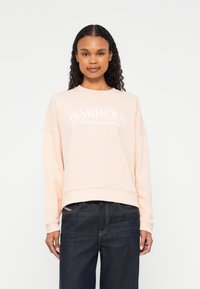 Heled särgis roosa pusa ümmarguse kaeluse, pikkade varrukate ja lõdva istuvusega. Rinnal on valge "BARBOUR INTERNATIONAL" tekst.