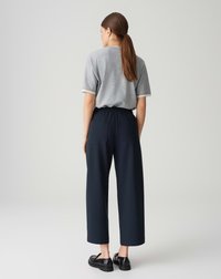 Chemise grise à manches courtes avec bordures blanches, associée à un pantalon à jambes larges taille haute bleu marine. Chaussures plates noires et texture lisse.
