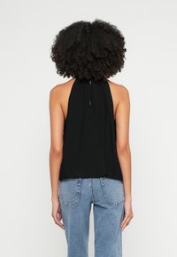 Juodas halterio tipo viršus su rakto skylutės formos iškirpte nugaroje, pagamintas iš lengvos medžiagos. Derinamas su aukšto liemens mėlynais džinsais, turinčiais užpakalines kišenes.