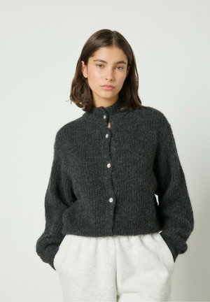 Kurze, dunkelgraue Strickjacke mit hohem Kragen und vorderer Knopfleiste. Verfügt über Perlenknöpfe und weite Ärmel, kombiniert mit hellgrauen Hosen.