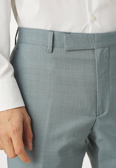 Pantaloni de culoare albastră deschisă, dintr-un material texturat, cu buzunare frontale și un design cu fața plată. Asortați cu o cămașă albă, evidențiind brâul.
