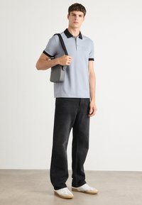 Lyseblå polo-shirt med marineblå krave, kombinert med svarte vide jeans og hvite sneakers, holder en grå crossbody-veske.