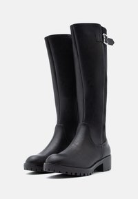 Bottes noires montant jusqu'au genou en cuir lisse avec un panneau texturé, ornées d'une boucle et d'une semelle épaisse à crampons.