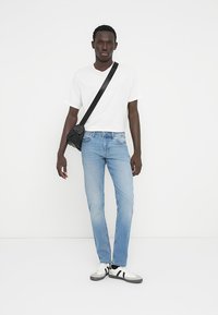 Ανοιχτό μπλε τζιν παντελόνι με ίσια γραμμή, συνδυασμένο με λευκό μπλουζάκι και μαύρη τσάντα ώμου. Τα παπούτσια έχουν λευκή βάση με μαύρες λεπτομέρειες.