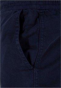 Dunkelblauer Stoff mit einer Nahaufnahme eines Taschenbereichs. Merkmale eine glatte Textur, gerade Nähte und einen elastischen Bund.