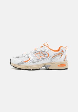 White athletic shoe with orange accents, mesh and synthetic upper, cushioned sole, featuring a subtle logo and textured details.
