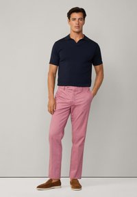 Mornarski polo majica kratkih rukava, ružičaste chinos hlače i smeđe cipele na slip-on. Polo majica ima ravni ovratnik; chinos hlače su krojene s glatkom teksturom.