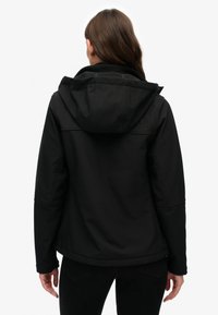 Schwarze Softshell-Jacke mit Kapuze, Reißverschlusstaschen und einer glatten Textur. Das Design ist modern mit Nahtdetails und einer schlanken Silhouette.