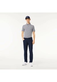 Randig polo skjorta i marinblått och vitt med krage, kombinerad med marinblå byxor och vita sneakers. Kappen har Lacoste-logotypen.