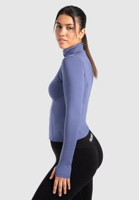 Langärmliges, hochgeschlossenes lila Sportoberteil aus glattem, elastischem Stoff, mit Nahtdetails und figurbetontem Design.