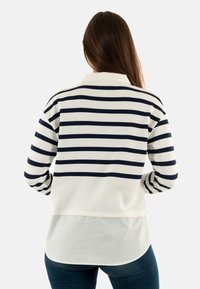 Camiseta de manga larga a rayas en azul marino y blanco con cuello tipo polo, que presenta un dobladillo en capas y una tela suave y texturizada.