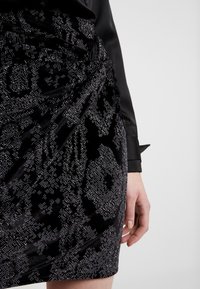 Svart sammetspets med ett ormskinsmönster. Har glänsande silverdetaljer, figurnära design och rynkad detalj vid midjan.