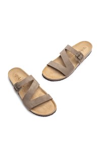 Bruine suède slidesandalen met gekruiste banden, voorzien van een metalen gesp en geprofileerde binnenzolen, geplaatst op een contrasterende donkere zool.