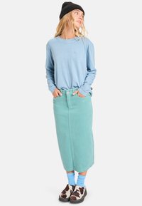 Ανοιχτό μπλε πουκάμισο με μακριά μανίκια, σε συνδυασμό με μια midi φούστα σε μέντα πράσινο χρώμα. Διαθέτει ίσια γραμμή, μπροστινές τσέπες και καφέ-άσπρα παπούτσια με σχέδια.