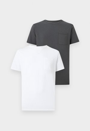 Twee effen crewneck t-shirts met voorzakken op de borst, één witte vooraan en één donkergrijze erachter op een lichte achtergrond.