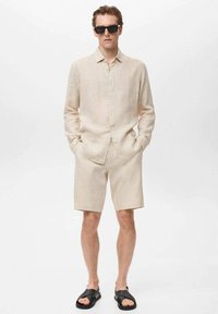 Beige linen shirt, buttoned, short sleeves; matching beige shorts; black sandals; black sunglasses. Smooth texture, relaxed fit.