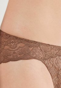 Brun spetsunderkläder med blommönster, mjuk textur och en genomskinlig midjeband, som framhäver detaljerat hantverk och design.