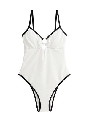 Bañador de una pieza blanco con acabado texturizado, tirantes y ribetes negros, con un diseño de corte en el busto y un adornoo circular dorado.