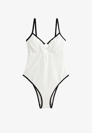 Bañador de una pieza blanco con acabado texturizado, tirantes y ribetes negros, con un diseño de corte en el busto y un adornoo circular dorado.