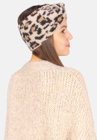 Un bandeau en imprim é léopard en tissu doux, présentant des nuances de beige, noir et marron, stylisé dans un design torsadé.